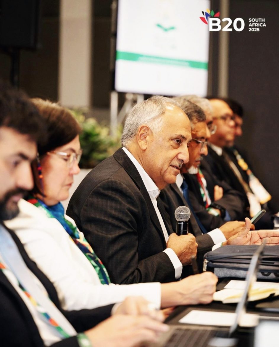 Cas Coovadia, the B20 Sherpa is holding a microphone at the B20 event on the sides of the G20 South Africa event. He is sitting alongside a group of other delegates (males and females). Cas Coovadia is the outgoing CEO of Business Unity South Africa (BUSA).